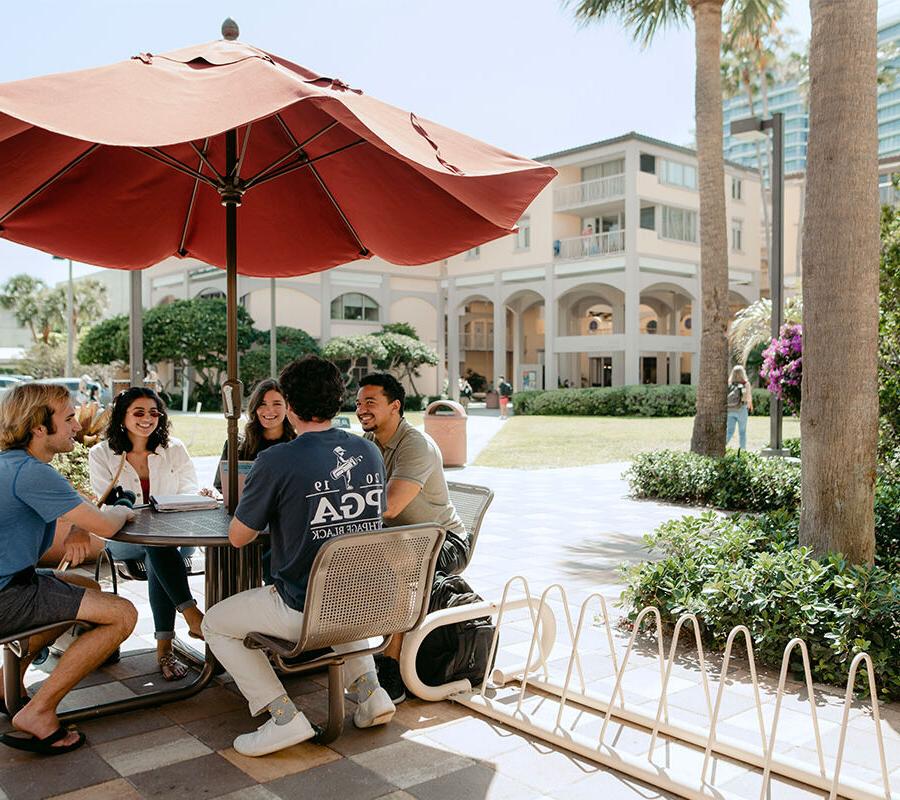 Intercultural studies students sit under an umbrella on campus.